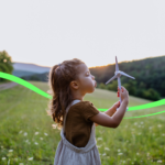 Criança da geração Z em um campo verde assoprando um aerogerador como se fosse um cata-vento.